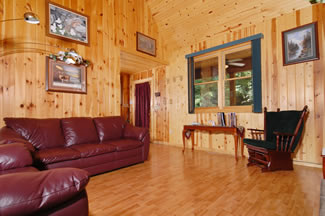 Living room with wood floors, wood walls, and a wood ceiling featuring a rocker that has a view of the living room and the dining room.